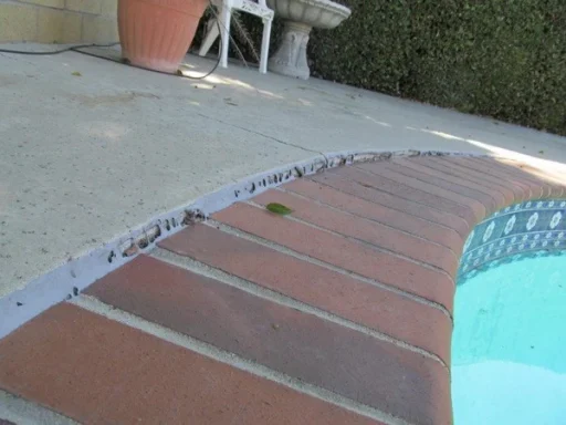 A pool edge with a concrete surface and a few scattered leaves nearby.