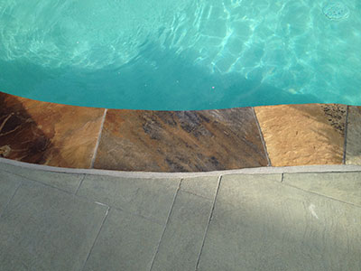 Textured stone border around a clear, blue swimming pool.