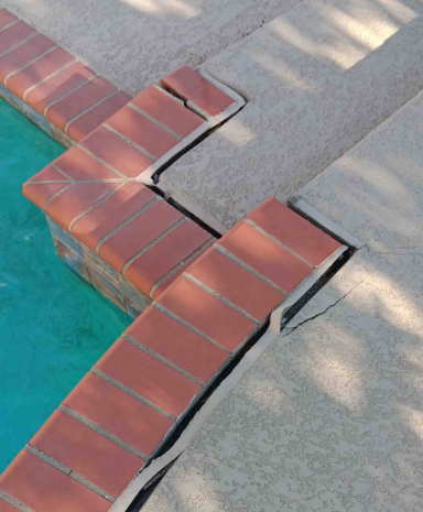 Cracked pool deck tiles near the edge of a swimming pool.