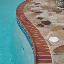 Curved stone patio surrounding a clear blue swimming pool.